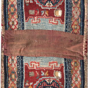 Narrow red textile with blue geometric medallions, light blue accents, fringe, and a central stitched maroon panel.