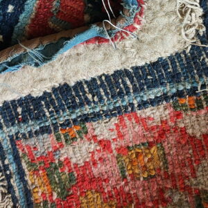 Folded section of a textured, low-pile rug showing red, navy, green, and yellow patterns with exposed backing.