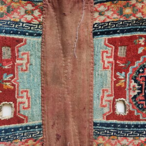 Red and blue patterned pile fabric borders a large, central reddish-brown patch with visible stitches and holes.