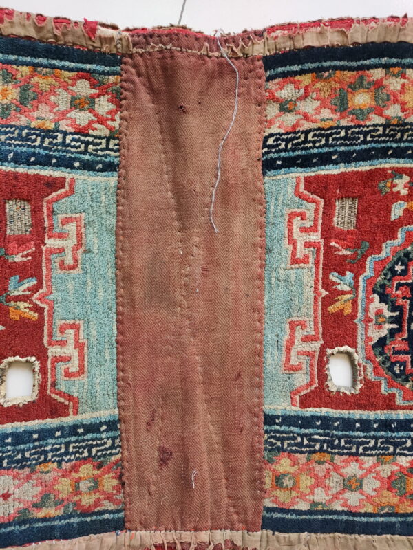 Red and blue patterned pile fabric borders a large, central reddish-brown patch with visible stitches and holes.