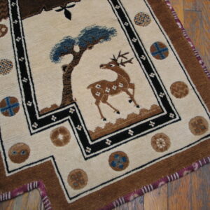 Cream rug with a central brown deer and blue tree motif, bordered in black and brown, resting on wood floor.