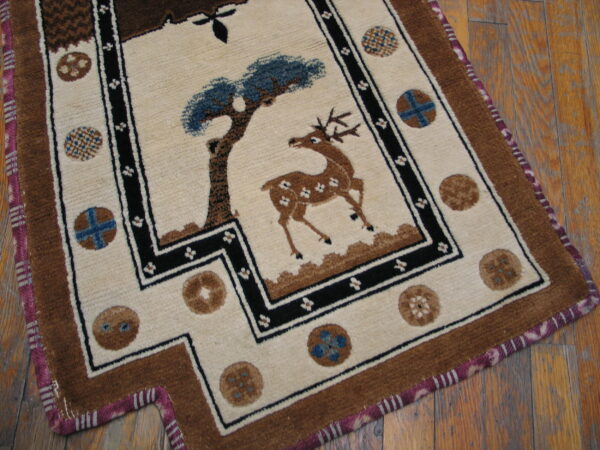 Cream rug with a central brown deer and blue tree motif, bordered in black and brown, resting on wood floor.