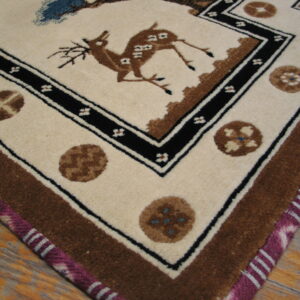 Cream rug corner with a brown deer and black border detail, featuring a magenta striped selvedge on wood.