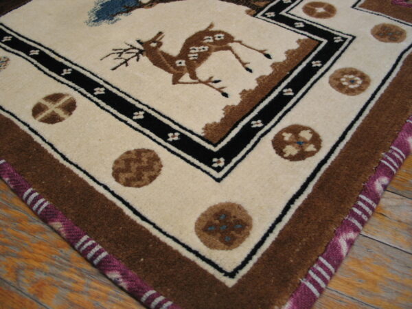 Cream rug corner with a brown deer and black border detail, featuring a magenta striped selvedge on wood.