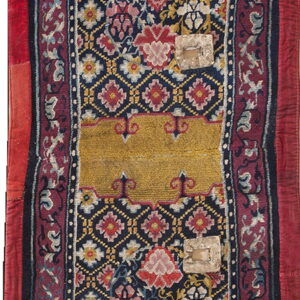 Blue rug fragment with detailed floral motifs, a gold central band, red borders, and surface patches.