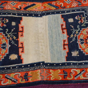 Navy and orange patterned rug with a split ivory and light blue center, showing visible wear and damage.