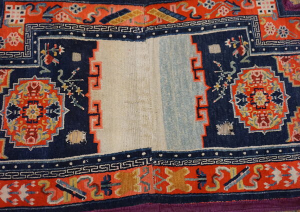 Navy and orange patterned rug with a split ivory and light blue center, showing visible wear and damage.
