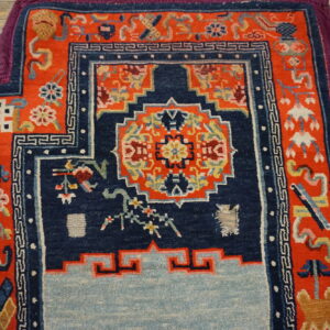 Geometric rug in navy, bright orange, and light blue with a purple edge sits on distressed wood floor.