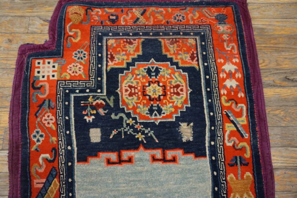 Geometric rug in navy, bright orange, and light blue with a purple edge sits on distressed wood floor.