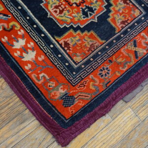 Navy and orange patterned rug corner with purple edging rests on distressed plank hardwood flooring.