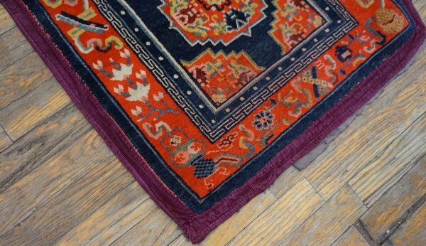 Navy and orange patterned rug corner with purple edging rests on distressed plank hardwood flooring.