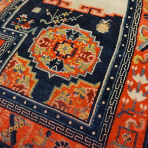 Vibrant orange and blue patterned rug showing geometric borders and floral motifs on a wooden floor.