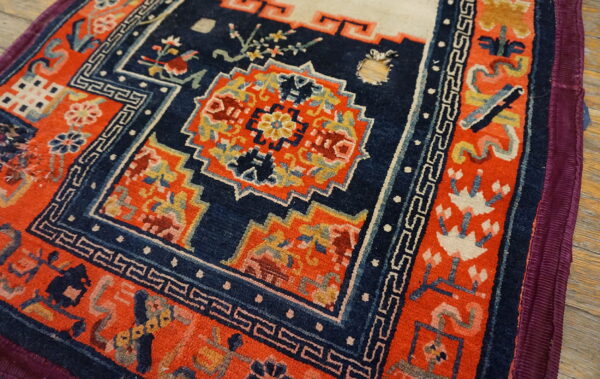 Vibrant orange and blue patterned rug showing geometric borders and floral motifs on a wooden floor.