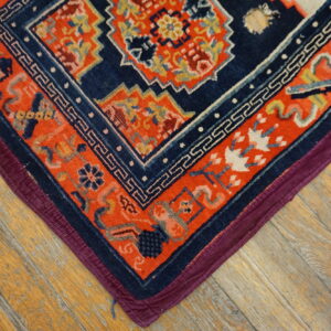 Navy and orange geometric rug corner featuring a meander border on worn wood flooring.