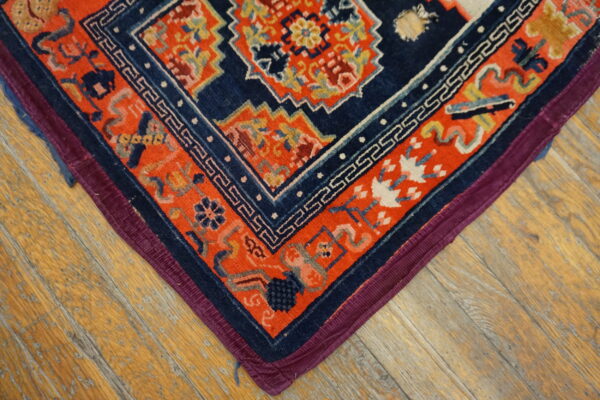 Navy and orange geometric rug corner featuring a meander border on worn wood flooring.