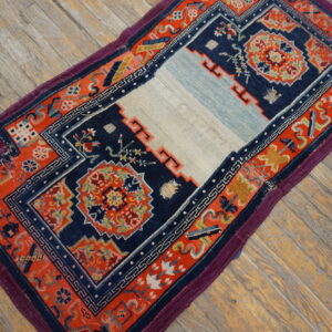 A small navy and coral-red geometric rug with a pale center stripe sits on rustic wooden plank flooring.