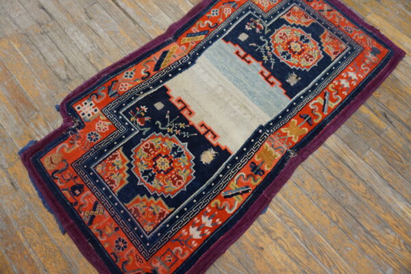 A small navy and coral-red geometric rug with a pale center stripe sits on rustic wooden plank flooring.