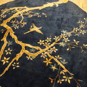 Dark blue high-pile rug with a gold branching tree, multi-colored blossoms, and a flying bird on wood floors.