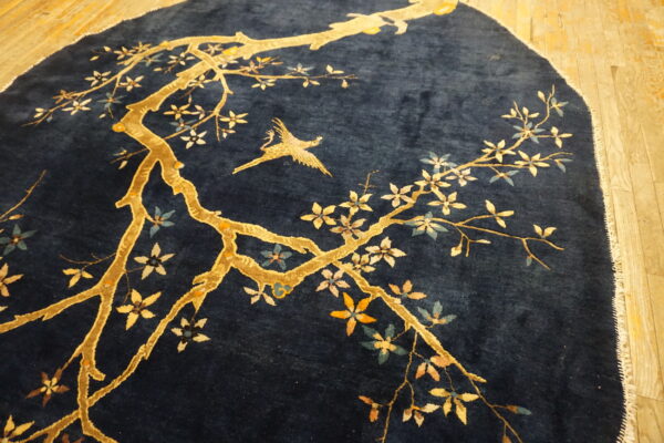 Dark blue high-pile rug with a gold branching tree, multi-colored blossoms, and a flying bird on wood floors.