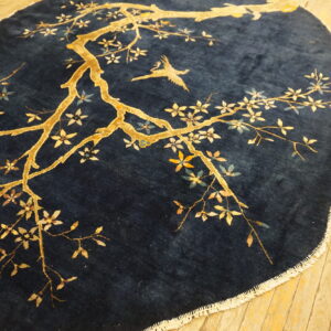 Deep pile blue rug with a gold blossoming branch and flying bird, resting on wood flooring.