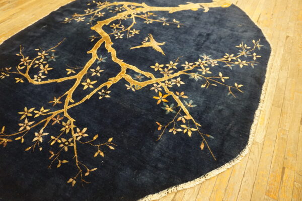 Deep pile blue rug with a gold blossoming branch and flying bird, resting on wood flooring.