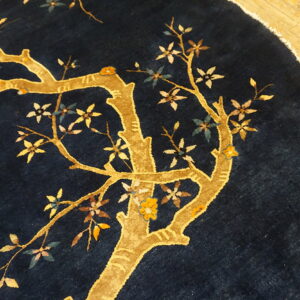 Round navy rug on a wood floor featuring a golden tree, multicolored blossoms, and a bird design.