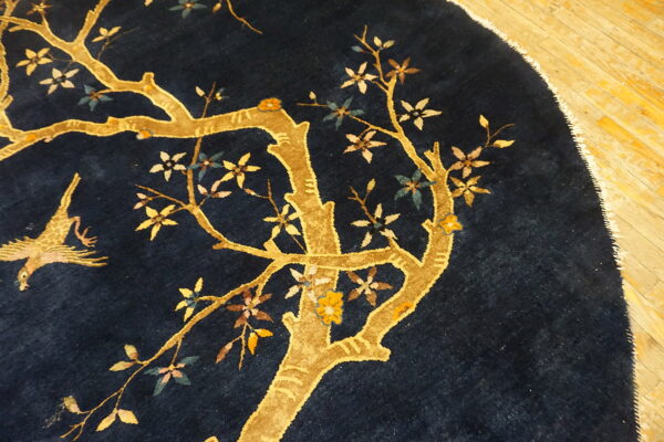 Round navy rug on a wood floor featuring a golden tree, multicolored blossoms, and a bird design.