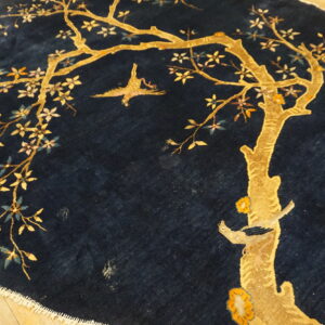A round, plush navy rug with a golden tree and bird motif on light wood flooring.
