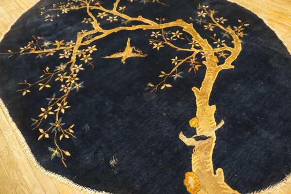 A round, plush navy rug with a golden tree and bird motif on light wood flooring.