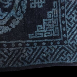 Close-up of a dark navy rug showing teal geometric borders and a scrolling pattern.