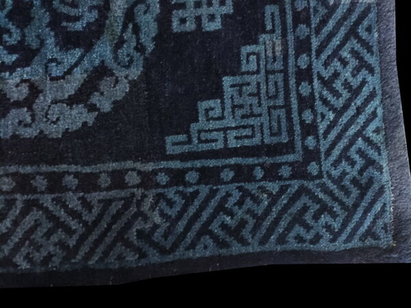 Close-up of a dark navy rug showing teal geometric borders and a scrolling pattern.
