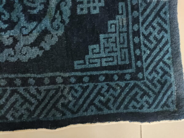 High-pile rug corner showing dark blue and teal geometric fretwork patterns on a light floor.