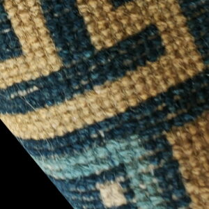 Highly textured close-up of a rug featuring an interlocking geometric pattern in tan, dark blue, and light blue.