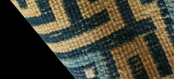 Highly textured close-up of a rug featuring an interlocking geometric pattern in tan, dark blue, and light blue.