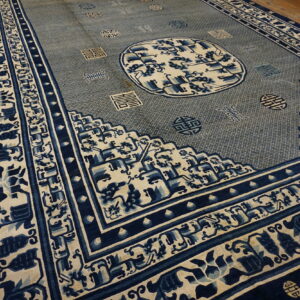 Large indigo and cream rug featuring a complex central medallion and symbolic borders on wooden flooring.