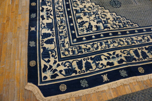 Navy and cream patterned rug corner with decorative borders and fringe on distressed wood flooring.