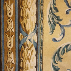 Close-up of an ornate rug featuring dark brown, blue, gold, and yellow scrollwork and floral borders.