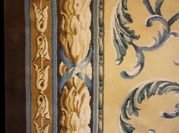 Close-up of an ornate rug featuring dark brown, blue, gold, and yellow scrollwork and floral borders.