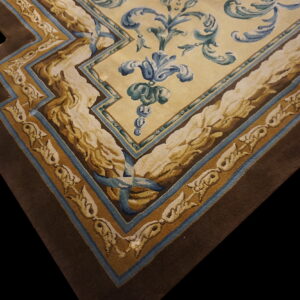 Ornate rug corner featuring a cream field with blue scrolling florals and wide brown and gold stepped borders.