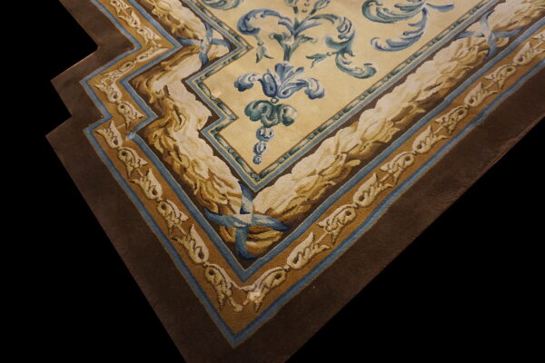 Ornate rug corner featuring a cream field with blue scrolling florals and wide brown and gold stepped borders.