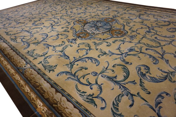 Traditional low-pile rug featuring blue and brown ornate scrolling patterns on a cream background and a layered border.