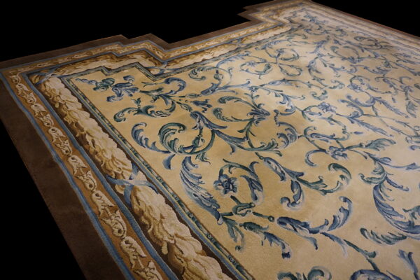 Pale gold rug with blue and green ornate scrolling designs, detailed borders, and a visible stepped corner.