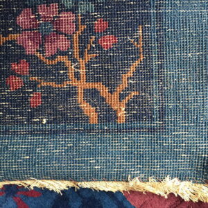 Flat woven rug edge displaying floral patterns in blue, magenta, and terracotta, with visible fringe over a dark rug.