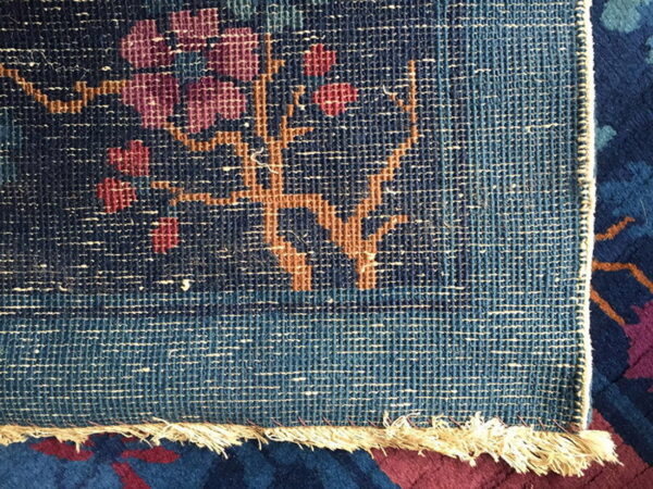 Flat woven rug edge displaying floral patterns in blue, magenta, and terracotta, with visible fringe over a dark rug.