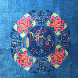 Bright blue rug detail featuring a central floral medallion encircled by pink flowers and script patterns.