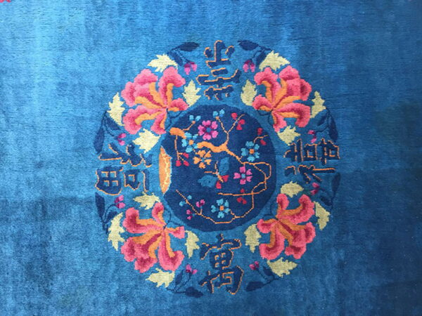 Bright blue rug detail featuring a central floral medallion encircled by pink flowers and script patterns.