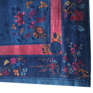 Dark blue rug with pink, orange, and teal floral motifs and a wide, solid coral-pink border band.