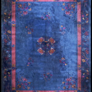 A deep blue rug featuring colorful floral patterns, a central medallion, and an inner mauve border band.