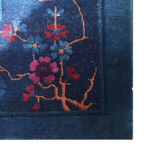 Dark blue high-pile rug detail showing magenta and teal blossoms connected by thin orange stems.