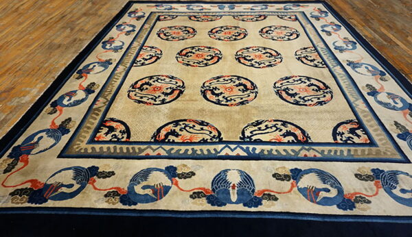 Beige area rug featuring blue and coral dragon medallions and a border of stylized blue cranes on a wood floor.